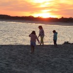 3 little girls enjoy exploring the shore at sunset