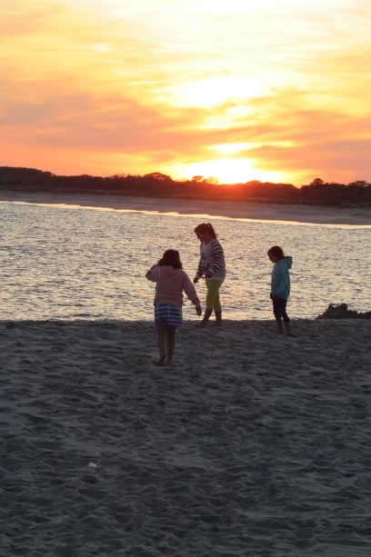 3 little girls enjoy exploring the shore at sunset